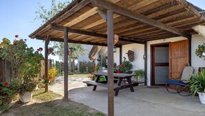 Un patio cubierto con una mesa y sillas de madera, rodeado de plantas en macetas y una estructura rústica de madera.