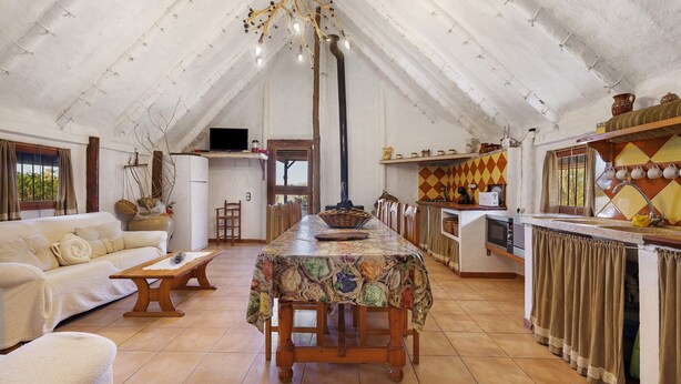 Un loft espacioso con techo alto, comedor con mantel estampado, cocina con salpicadero de azulejos y una zona de estar acogedora con sofá y sillones.