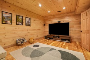 A wooden-paneled room with a flat-screen TV on a wooden stand, a plush rug, and a small stuffed animal on the floor.