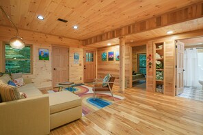 A wooden cabin interior with a sofa, chair, and a rainbow-patterned rug.