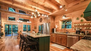 A wooden cabin interior with a kitchen, dining area, and bar seating. - The Leaflet | Hocking Hills, Swim Spa, Theater (Laurelville)