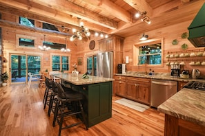 A wooden cabin interior with a kitchen featuring a large island, bar stools, a refrigerator, and a dishwasher.