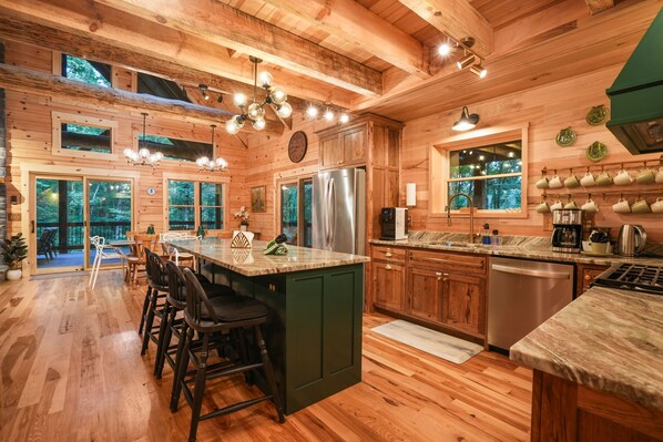 A wooden cabin interior with a kitchen featuring a large island, bar stools, a refrigerator, and a dishwasher.