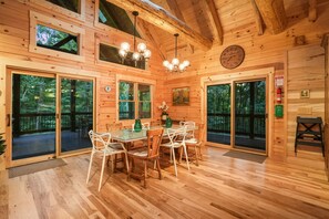 A wooden cabin with a dining area featuring a glass table and chairs, large windows, and a wooden ceiling. - The Leaflet | Hocking Hills, Swim Spa, Theater (Laurelville)