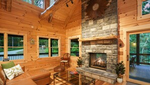A cozy cabin interior with a stone fireplace, wooden walls, and a glass coffee table. - The Leaflet | Hocking Hills, Swim Spa, Theater (Laurelville)