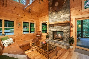 A cozy cabin interior with a stone fireplace, wooden walls, and a leather sofa.