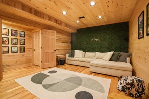 A cozy room with wooden walls, a green wall with 'The Leadet' text, a white sofa, and a cow-shaped decoration.