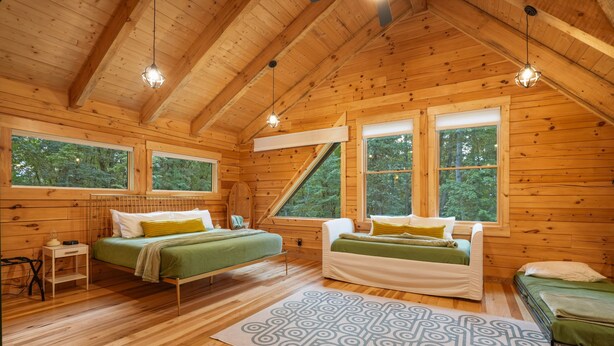 A wooden cabin bedroom with two beds, a nightstand, and a window overlooking a forest. - The Leaflet | Hocking Hills, Swim Spa, Theater (Laurelville)