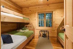 A cabin with bunk beds, a window with a view of trees, and a small table with a chair.