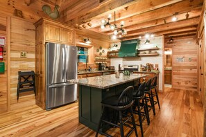 Una cocina de estilo cabaña de madera con un refrigerador de acero inoxidable, armarios de madera y una isla de mármol con taburetes de bar.