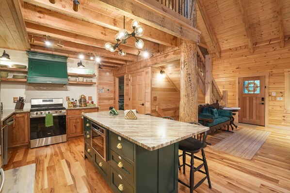 A spacious kitchen with wooden floors, a central island, and a staircase leading to a loft area.