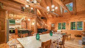 A wooden cabin interior with a dining area, kitchen, and a staircase leading to an upper level. - The Leaflet | Hocking Hills, Swim Spa, Theater (Laurelville)