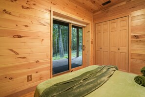 Una habitación de cabaña de madera con una cama, una puerta corredera a una terraza y un armario.