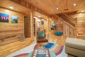 A wooden interior with a staircase, a sofa, a coffee table, and a television. - The Leaflet | Hocking Hills, Swim Spa, Theater (Laurelville)