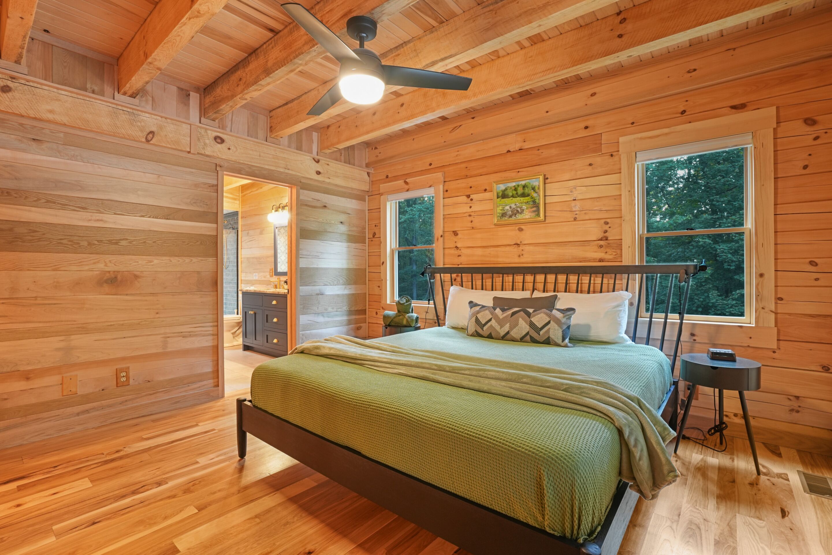 A wooden cabin bedroom with a bed, a nightstand, a ceiling fan, and two windows.