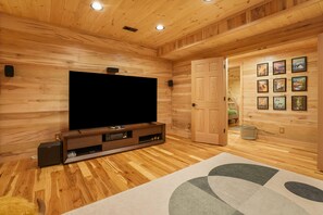 A wooden-paneled room with a large flat-screen TV on a wooden stand, a door leading to another room, and a wall with framed pictures.