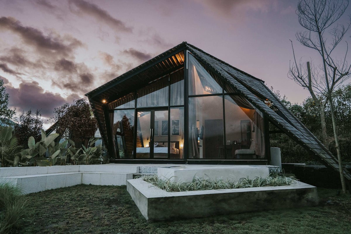 Una casa moderna con grandes ventanales, un techo inclinado y una jardinera de concreto al frente.