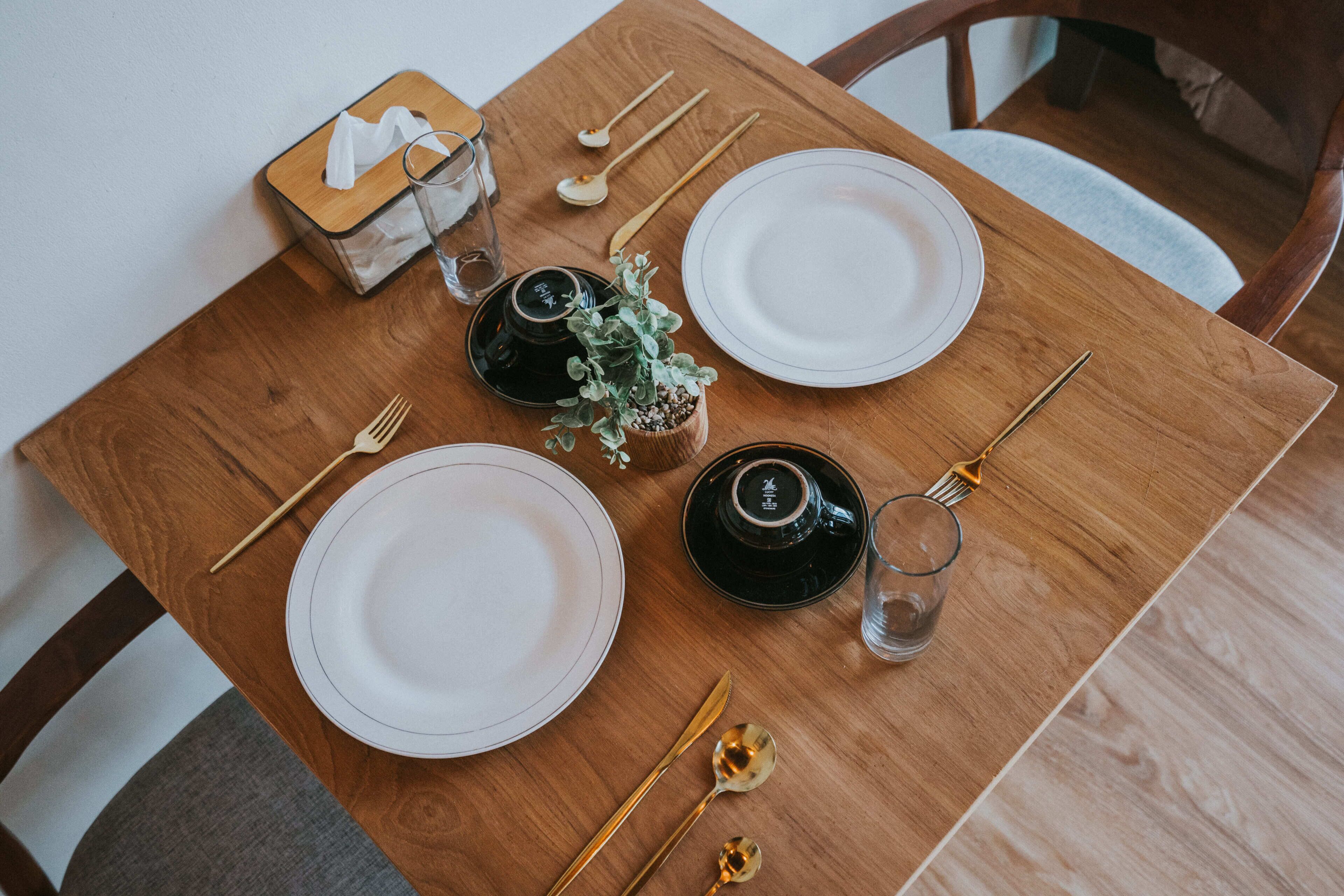 A neatly set dining table with plates, cutlery, glasses, and a tissue box.