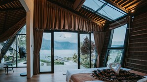 A bedroom with a large bed, a heart-shaped towel arrangement, and a view of a lake through large windows. - Skylake Villa (Kintamani)