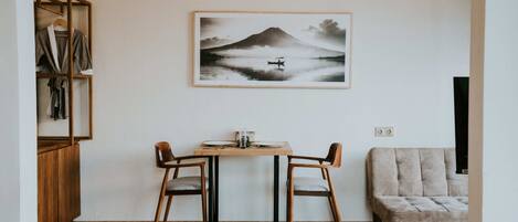 Ein Zimmer mit Holzboden, einem Tisch mit Stühlen, einer Couch, einem gerahmten Bild von einem Berg und einem Kleiderschrank.