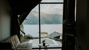 A room with a large window, a sofa, a small table with a plant, and a television. - Skylake Villa (Kintamani)