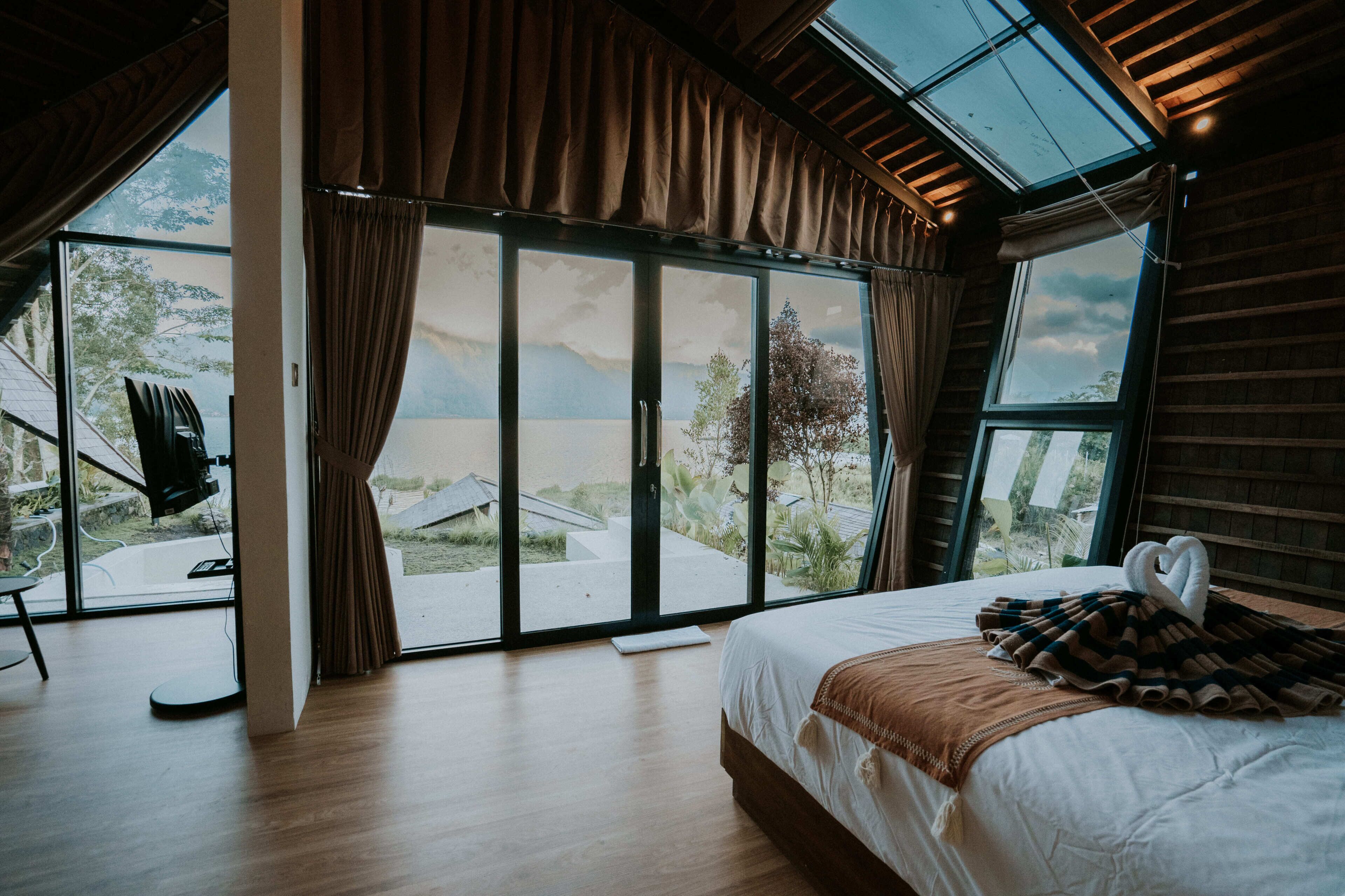 A bedroom with a large bed, a view through a sliding glass door, and a wooden ceiling.