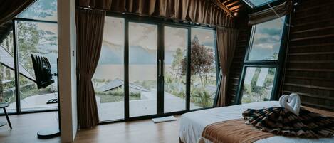 A bedroom with a large bed, a view through a sliding glass door, and a wooden ceiling.