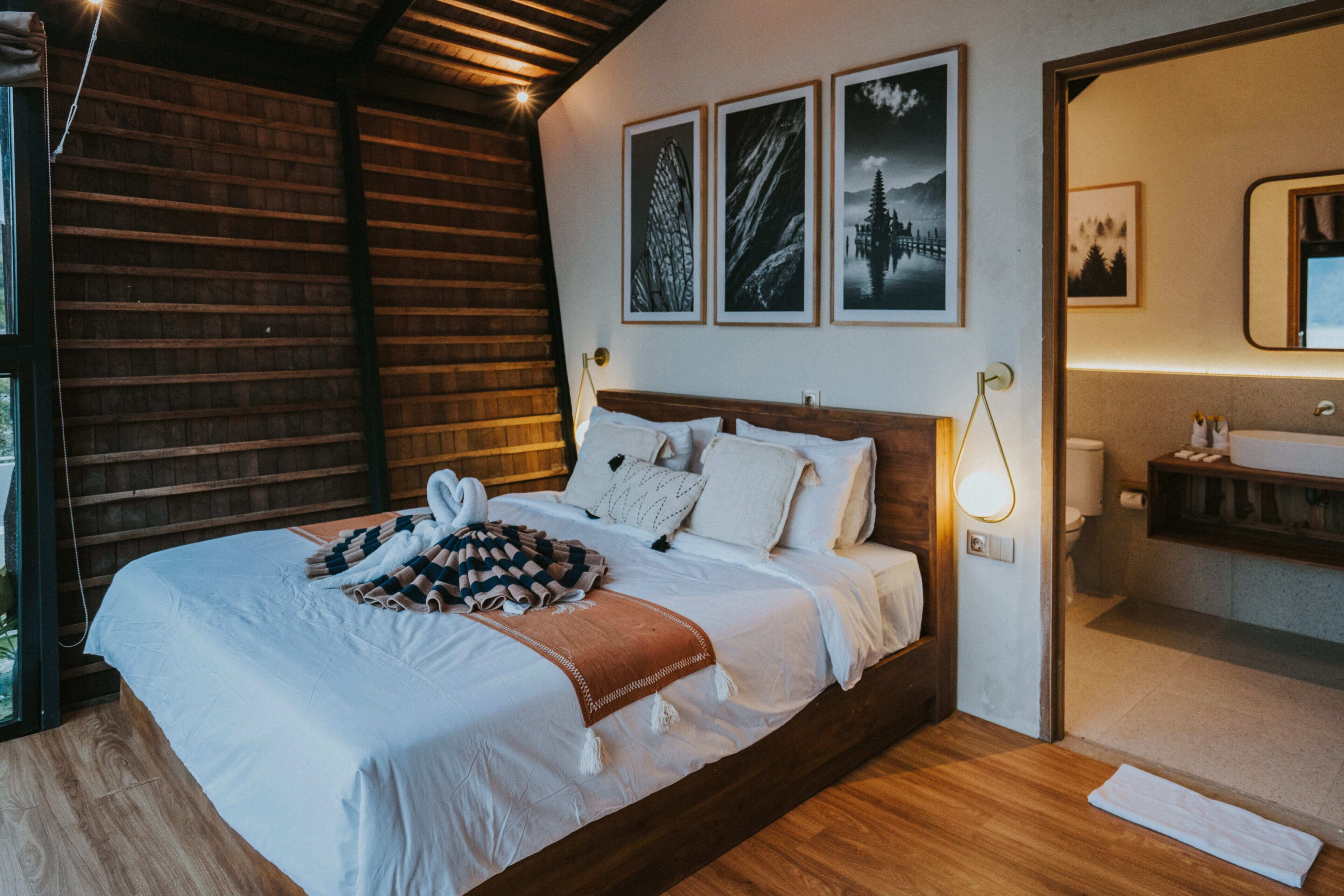 Une chambre à coucher avec un lit en bois, une lampe de chevet et des œuvres d’art encadrées accrochées au mur.