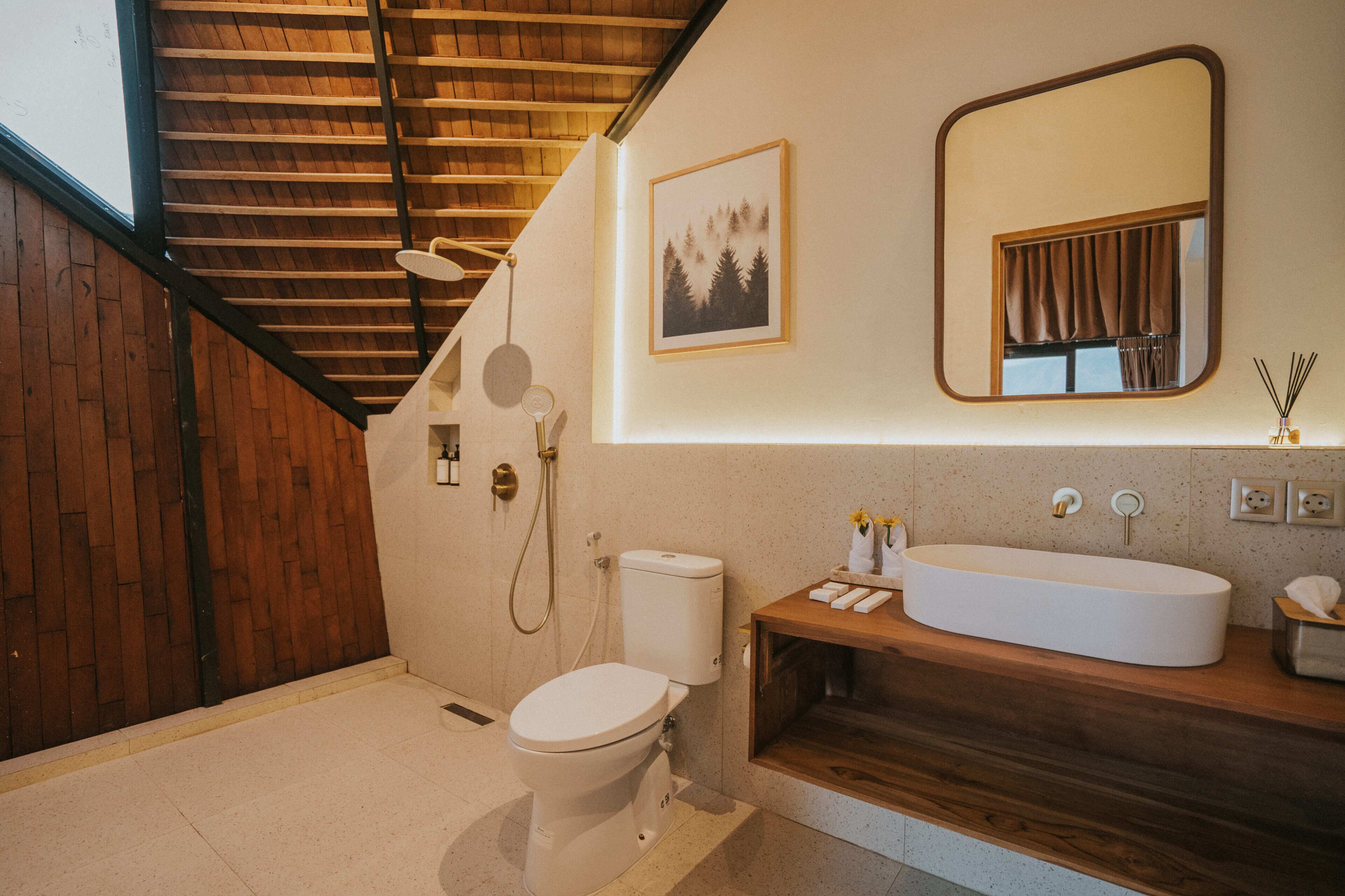 A bathroom with a toilet, shower, sink, mirror, and a framed picture on the wall.