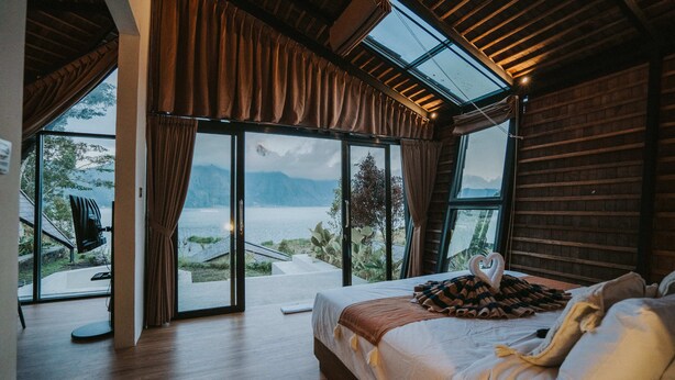 A bedroom with a large bed, a TV, and a view of a lake and mountains. - Skylake Villa (Kintamani)