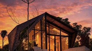 A modern house with a glass facade, surrounded by greenery and a stone base. - Skylake Villa (Kintamani)