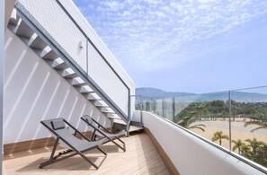 Varanda com duas espreguiçadeiras, uma escadaria e vista para a praia e montanhas.