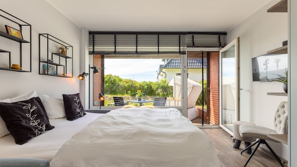 Ein modernes Schlafzimmer mit einem großen Bett, einer Sitzecke und Blick auf den Garten.