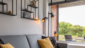 Ein modernes Wohnzimmer mit einem grauen Sofa, schwarzen Metallregalen und zwei Wandleuchten.