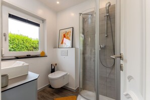 Et moderne badeværelse med et glasbadeværelsesafskærmning, et hvidt toilet og en håndvask med et vindue over.