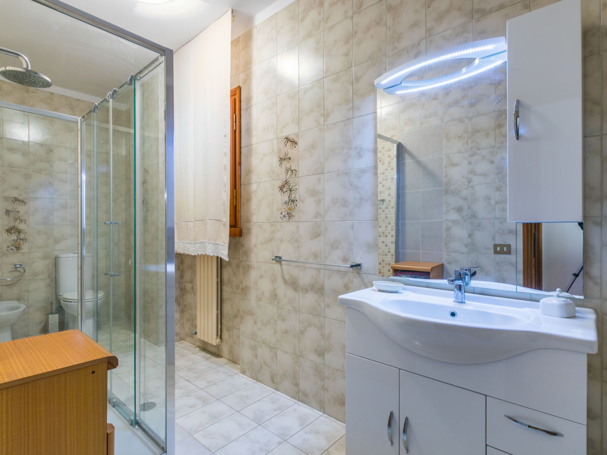 Un baño moderno con cabina de ducha de vidrio, un lavabo blanco con espejo y un mueble de tocador de madera.