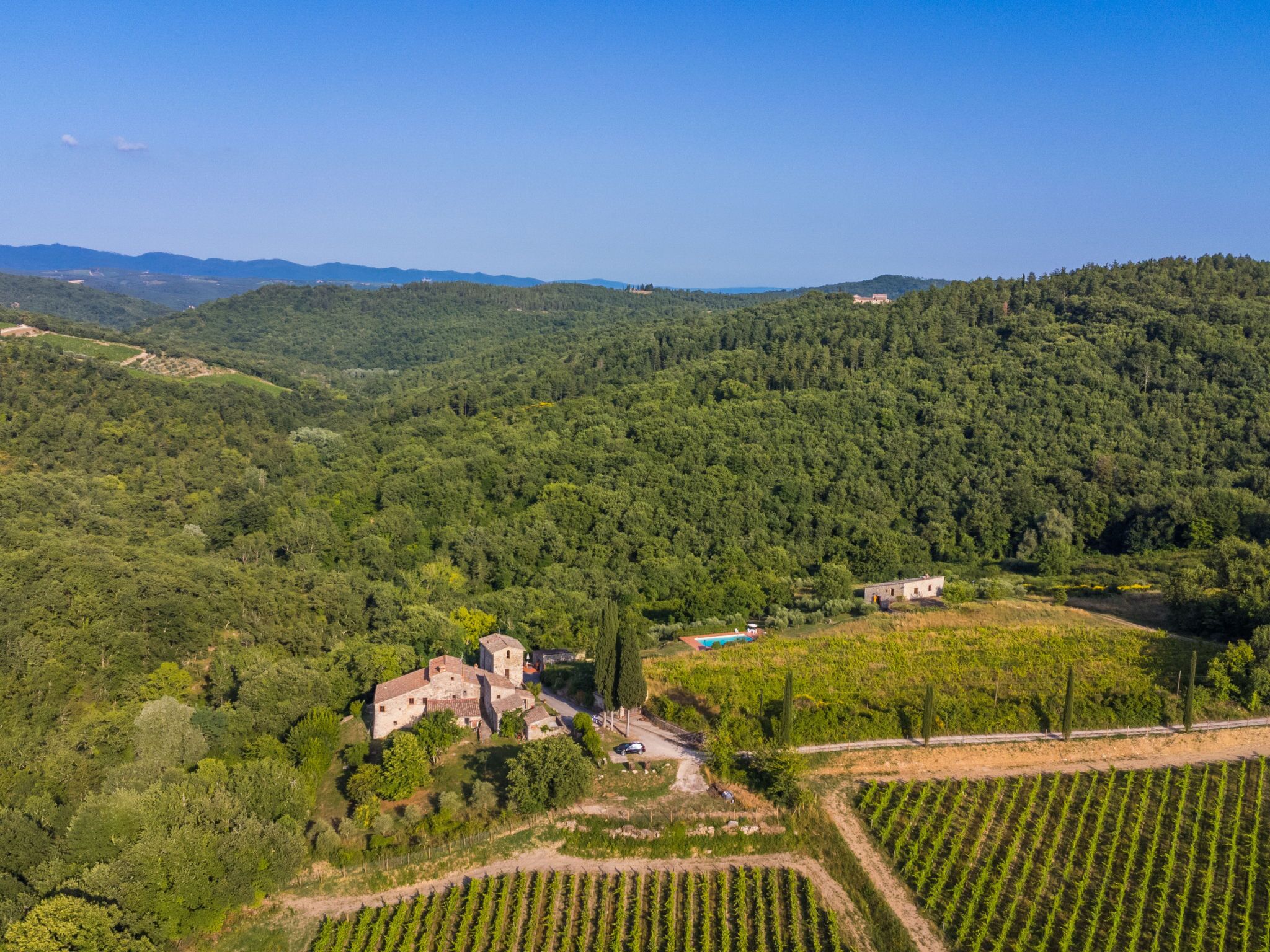 An aerial view of a historic stone building surrounded by lush greenery and vineyards.