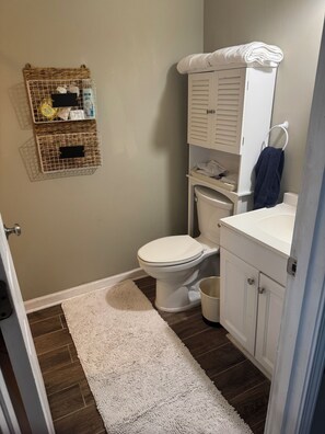 A bathroom with a toilet, a white sink, a towel rack, and a white rug.
