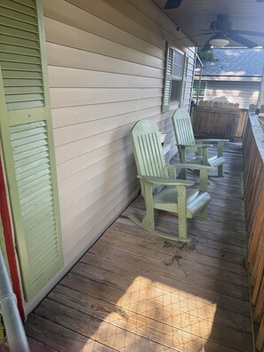 En inglasad veranda med två gröna Adirondack-stolar, ett trädäck och en vit yttervägg.
