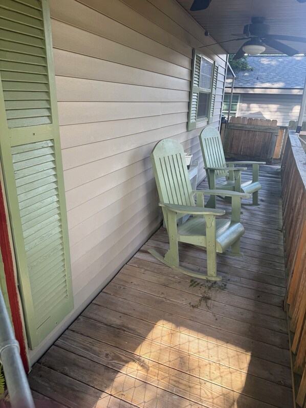 A covered porch with two green Adirondack chairs, a wooden deck, and a white exterior wall.