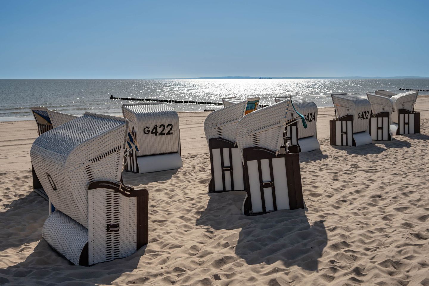 Sedie da spiaggia numerate disposte su una spiaggia sabbiosa, con l'oceano sullo sfondo.