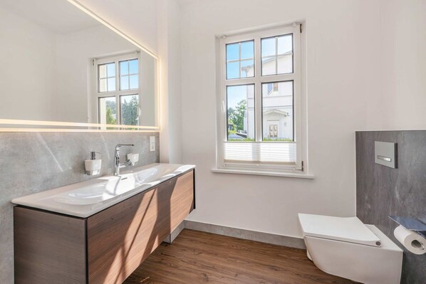 Un baño moderno con tocador doble, inodoro y ventana con persianas.
