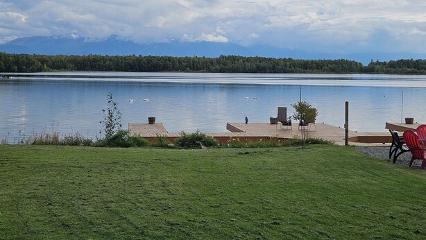 A lakeside view with a wooden dock, chairs, and a grassy area. - Modern Lake Lucille Lakefront, Whole 5 bedroom house, Private dock & games
 (Wasilla)