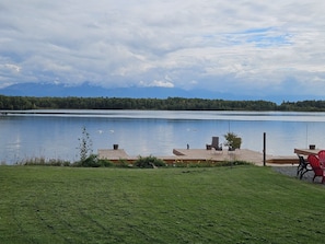 A lakeside view with a wooden dock, chairs, and a grassy area.