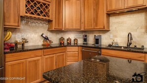 A kitchen with wooden cabinets, a granite countertop, a wine rack, and various kitchen appliances. - Modern Lake Lucille Lakefront, Whole 5 bedroom house, Private dock & games
 (Wasilla)