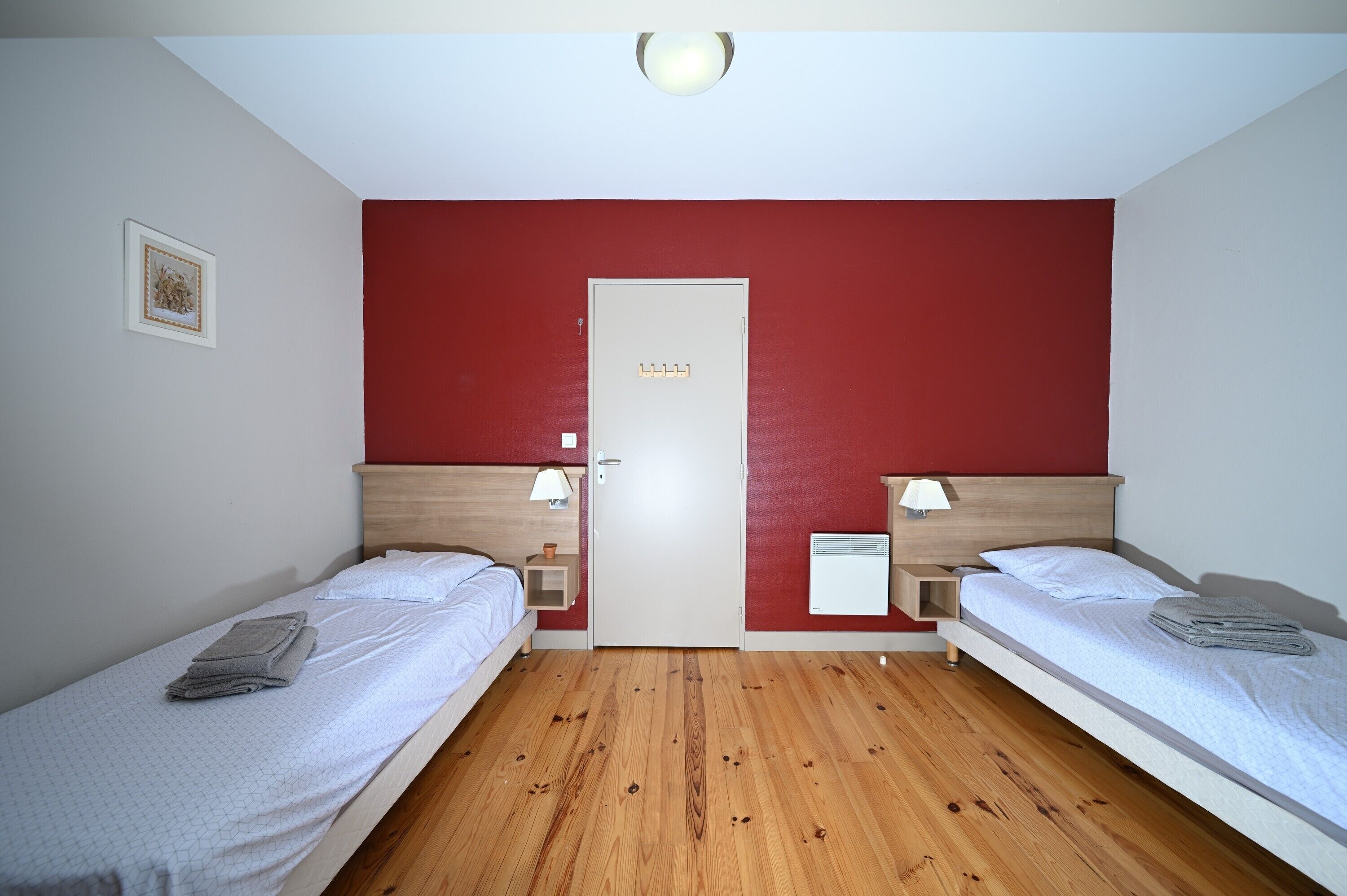 Ein Zimmer mit zwei Einzelbetten, einer Tür, einer Lampe und einem kleinen Nachttisch mit Leuchte.