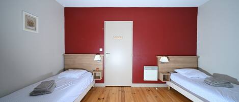 Ein Zimmer mit zwei Einzelbetten, einer Tür, einer Lampe und einem kleinen Nachttisch mit Leuchte.