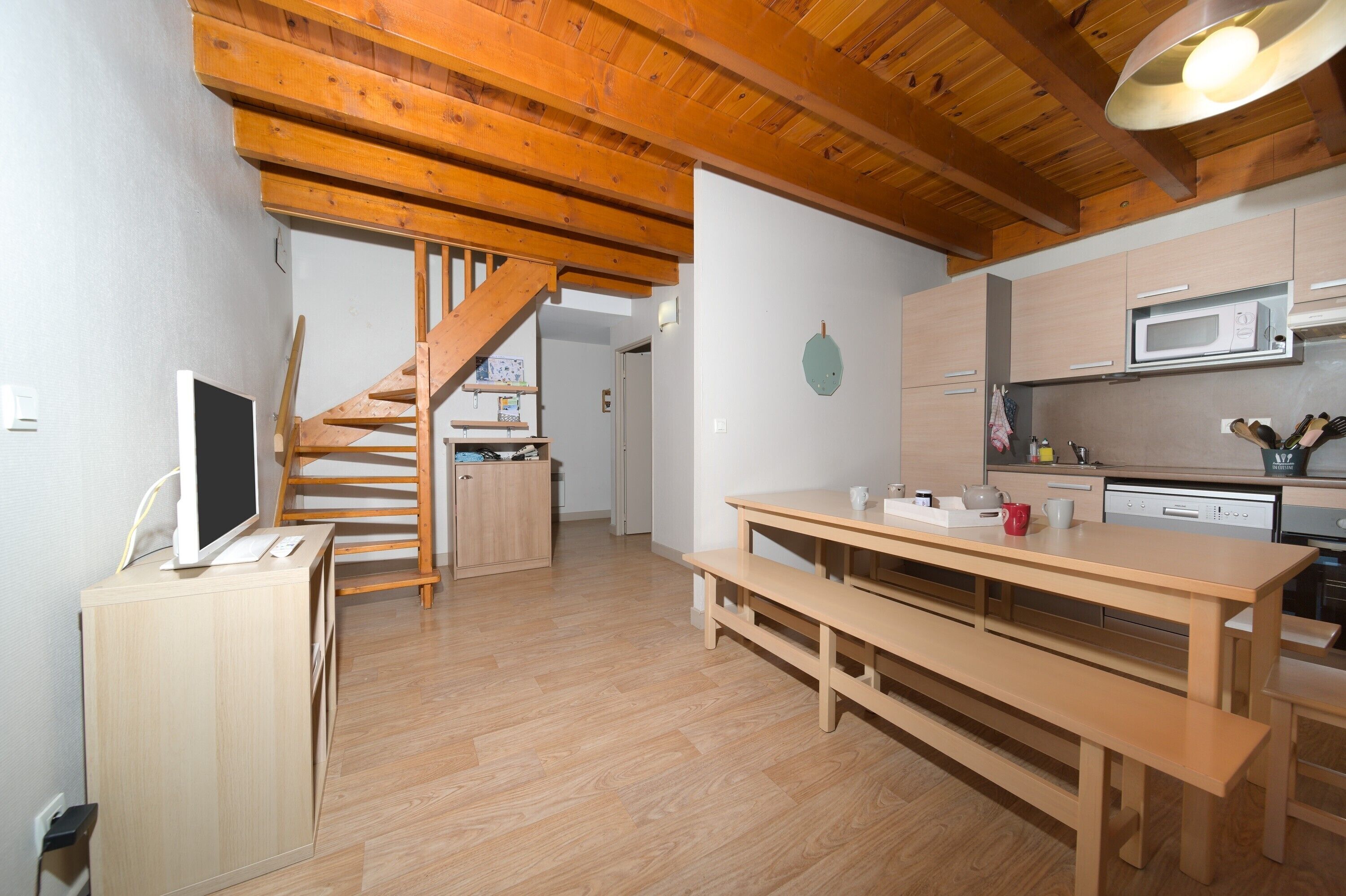 Une cuisine avec des poutres en bois, une table à manger et un escalier.
