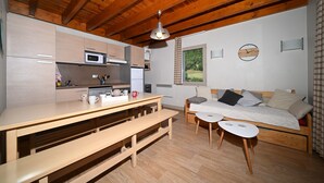 Un espacio habitable compacto con kitchenette, vigas de techo de madera, una mesa de comedor, un sofá y una ventana pequeña con vistas.