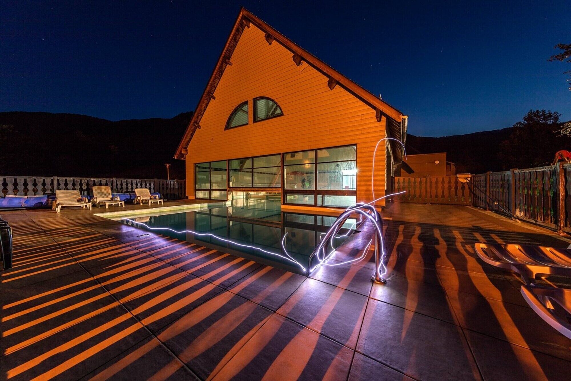 Una casa con piscina, terraza de madera y un ventanal grande.